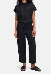 Camicia nera in lino a maniche corte con chiusura frontale a bottoni, abbinata a pantaloni neri a gamba larga con coulisse in vita. Sandali neri flat.