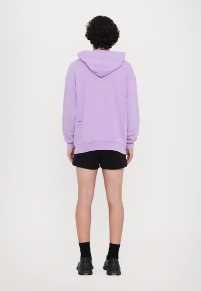 Sweatshirt roxa com capuz, de mangas longas, corte descontraído, detalhe de fenda lateral, combinado com calções pretos e calçado escuro.