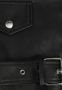 Le matériau en cuir noir présente une poche cousue avec un bouton-pression en argent et une ceinture avec une boucle en métal et des œillets décoratifs.