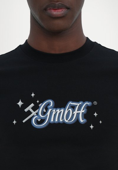 Tricou din bumbac negru, cu un logo grafic mare în nuanțe de albastru și argint "GmbH" accentuat cu stele și un design decorativ cu uneltele încrucișate.
