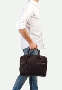 Braune Lederaktentasche mit zwei oberen Griffen, einem Reißverschluss-Hauptfach und einer Vordertasche. Verfügt über eine dezente, strukturierte Oberfläche und ein Etikett.