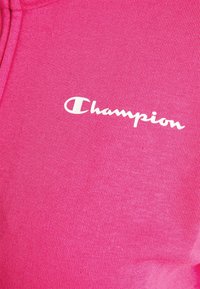Felpa rosa in morbido tessuto, con texture a coste, cappuccio e logo bianco "Champion" sul petto.