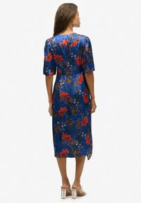 Een blauwe satijnen jurk met korte pofmouwen, voorzien van een bloemenpatroon in rood en groen. De jurk heeft een mid-lengte zoom met een zijsplit.