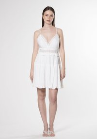 Vestido mini blanco con escote en V, borde de encaje, tirantes finos ajustables y dobladillo con volantes en capas. Tejido ligero con una textura suave.