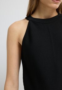 Zwarte mouwloze top van ribstof, met een hoge hals en een asymmetrisch schouderontwerp. Gelijke textuur zonder patronen.