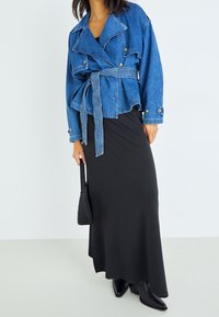 Jeansjacka med bältad midja, med stora slag och gyllene knappar. Kombinerad med en svart, figursydd maxiklänning och svarta klackstövlar.