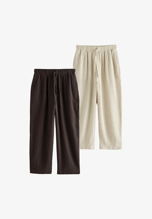 Twee paar gestructureerde, loszittende broek met trekkoord, één in donkerbruin en één in licht beige, naast elkaar weergegeven op een witte achtergrond.