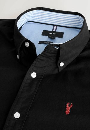 Sort bomuldsbluse med hvide knapper, krave-design, broderet rød hjort-logo på brystet og indvendig krave i lyseblå striber.
