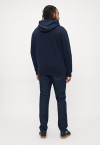 Hoodie bleu marine avec capuche à cordon, coupe décontractée. Porté avec un jean en denim foncé et des baskets noires avec une semelle en caoutchouc beige.
