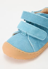 Lysblå ruskindsko med to Velcro-stropper, gummisål i beige og syet detalje. Runde tådesign for komfort og støtte.