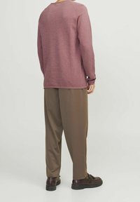 Langärmeliger, dunkelroter Pullover mit strukturierter Oberfläche, kombiniert mit locker sitzenden braunen Hosen und dunklen Schuhen. Lässiger, entspannter Stil.