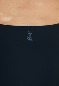 Zwart rekbaar stof met een zachte textuur, met een grijze logo op de tailleband. Het ontwerp is minimalistisch en aansluitend.