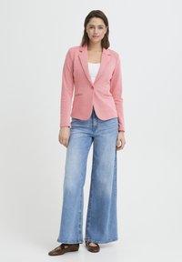 Blazer ajusté rose clair avec revers crantés, fermeture à un bouton, associé à un jean large bleu clair et des ballerines marron.