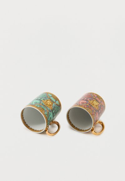 Δύο διακοσμητικά κεραμικά φλιτζάνια με χρυσές λαβές, ένα τιρκουάζ και ένα ροζ, το καθένα με σχέδιο χρυσού κεφαλιού λιονταριού και περίτεχνα μοτίβα.