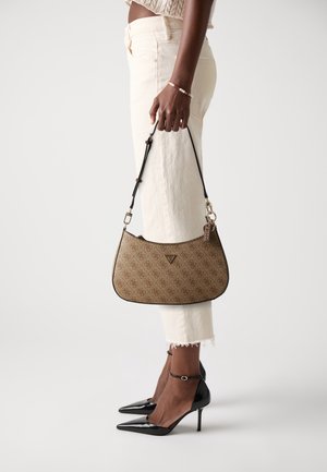 Sac à main marron à motif avec une forme incurvée, une sangle noire et des accessoires dorés ; porté avec un pantalon crème et des chaussures noires à talons hauts.