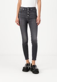 Dżinsy typu skinny o wysokim stanie w ciemnoszarym denimu, z pięcioma guzikami, bocznymi kieszeniami i dopasowanym krojem. Zestawione z czarnymi butami na platformie.