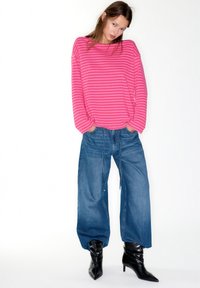 Lyserød og stribet bluse med lange ærmer kombineret med løstsiddende blå jeans og sorte spidse ankelstøvler. Glat tekstur, afslappet pasform.