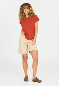 Rød T-shirt med korte ærmer, beige elastik-liv shorts med lommer og brune klipklapper. Simpelt design, afslappet pasform, blød tekstur.