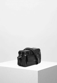 Svart läderväska med en texturerad krokodilsmönster. Har dragkedjestängning, justerbar axelrem och en framficka.