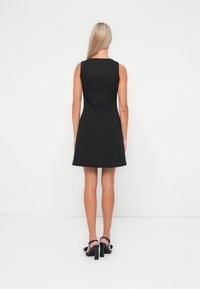 Black sleeveless dress with vertical ribbed texture, fitted bodice, and flared skirt. Paired with black heeled sandals featuring bows.