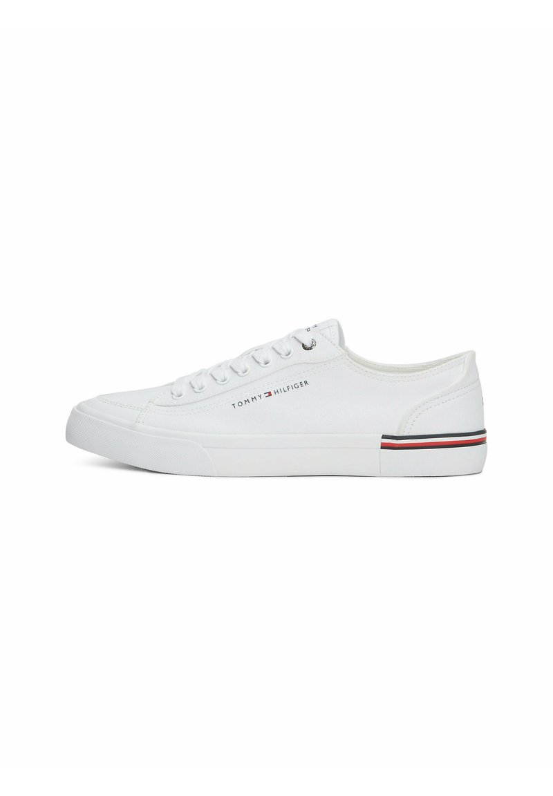 Zapatilla de lona blanca con puntera redonda, diseño de seis ojales para cordones, que presenta un logo de marca y un acento a rayas en el lateral de la suela.
