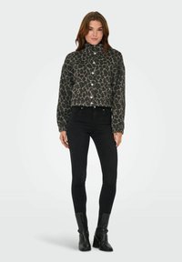 Geknipt jasje met een zwart en grijs panterprint, knoopsluitingen en een hoge kraag, gecombineerd met zwarte skinny jeans en laarzen met een hak.