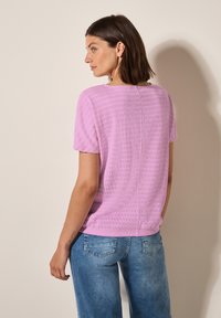 Růžový top s krátkým rukávem, který má texturovaný vzor, spárovaný s modrými džínami s mírným opráním a detaily na zadní kapse.