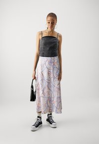 Svart denimcropped topp med perledetaljer, kombinert med et pastellfarget paisleymønster skjørt. Tilbehør inkluderer en svart håndvogn og høyhælte sneakers.