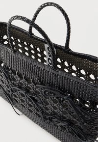 Μαύρη υφασμένη τσάντα χειρός με πλεκτές λαβές και διακοσμητικούς πλεκτούς φιόγκους στο μπροστινό μέρος, που δείχνει μια εσωτερική ετικέτα.