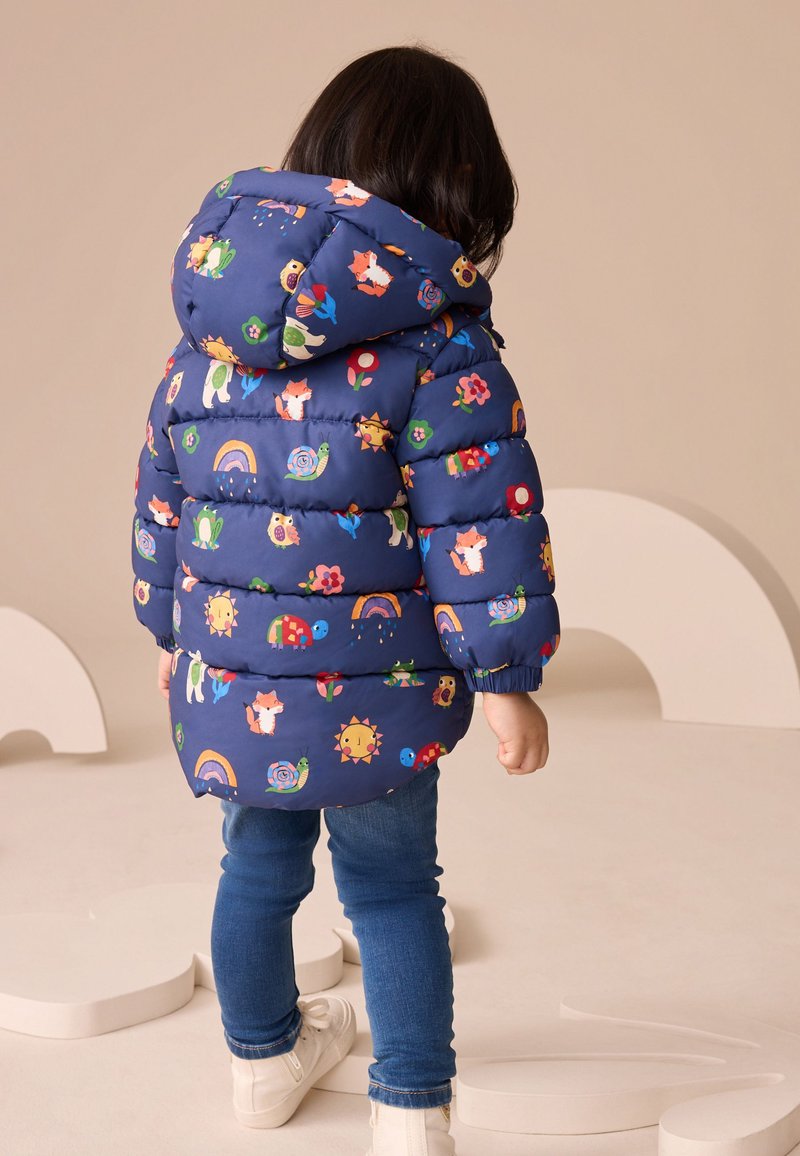 Granatowa pikowana kurtka z kolorowymi wzorami zwierząt i kwiatów, z kapturem i ściągaczami na rękawach. Połączona z niebieskimi dżinsami i białymi butami.