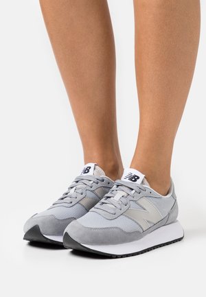 Grå sneakers med en blanding af mesh og ruskindsmaterialer, med en sort gummisål, hvide accenter og et syet design.