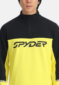 Pullover in fleece nero e giallo con zip e maniche lunghe. Caratterizzato da un colletto alto e un grande logo "SPYDER" nero sul petto.