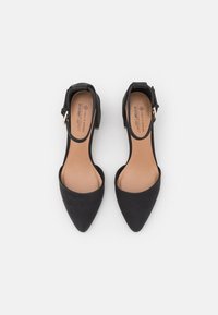 Black, pointed-toe heels with a smooth texture and ankle strap. Interior features beige padding. Minimalist design with a low block heel.