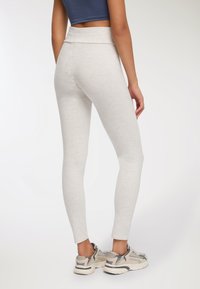 Jasnoszare legginsy o dopasowanym kroju i szerokiej talii. Wykonane z miękkiego materiału, zwężające się na kostce, zestawione z trampkami.