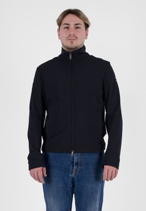 Giacca zip-up nera realizzata in tessuto liscio, con colletto alto, tasche laterali e una linea aderente. Indossata con jeans in denim blu.