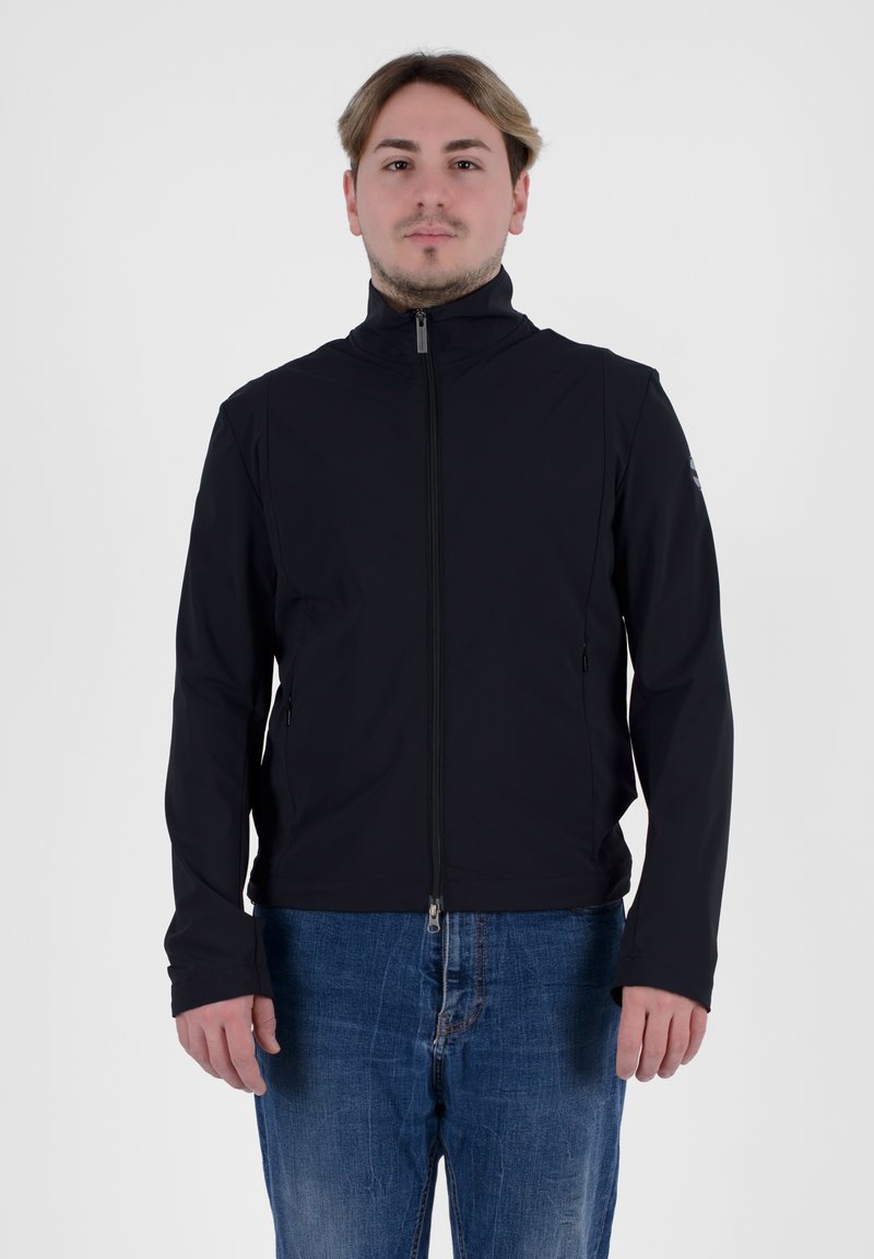 Giacca zip-up nera realizzata in tessuto liscio, con colletto alto, tasche laterali e una linea aderente. Indossata con jeans in denim blu.