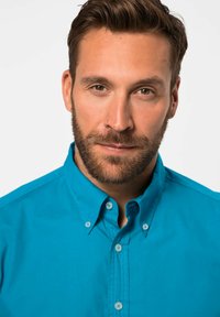 Camicia azzurra con colletto a punta, caratterizzata da una texture liscia, cuciture visibili e bottoni cuciti sul davanti.
