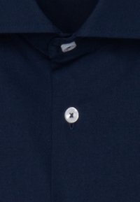 Camicia blu navy con bottoni, realizzata in un tessuto dalla superficie liscia, caratterizzata da un singolo bottone argentato al colletto e una forma classica.