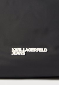 Μαύρη υφασμάτινη τσάντα ώμου με λευκό ανάγλυφο κείμενο "KARL LAGERFELD JEANS", με λεία υφή και μινιμαλιστικό σχεδιασμό.