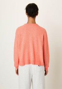 Koralen roza pleteno pulover s okroglim izrezom, spušenimi rameni in rebrastimi manšetami. Mehka tekstura in rahlo skrajšana zasnova.