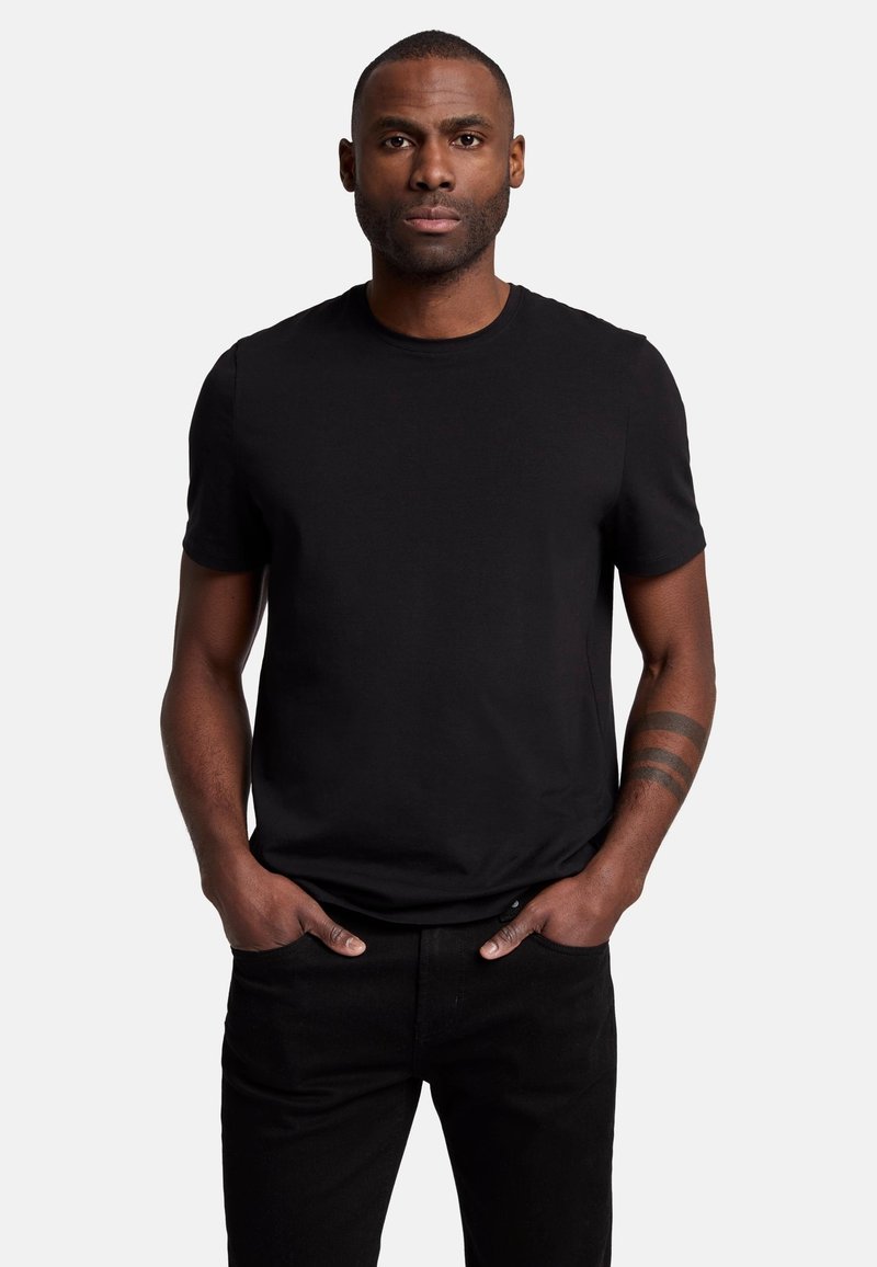 T-shirt nera a maniche corte in cotone, caratterizzata da un collo a giroclassico e una vestibilità rilassata. Indossato con jeans neri slim.