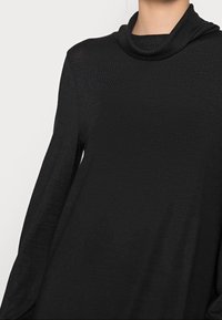 Černý pletený svetr s vysokým, ribovaný límcem a dlouhými rukávy. Tkanina má hladkou strukturu a volný střih.