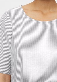 Blouse rayée avec un col rond, manches courtes, en tissu doux avec des rayures verticales gris et blanc, texture lisse.