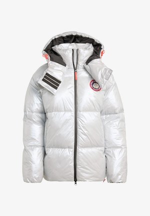 Srebrna kurtka puchowa z kapturem, wyposażona w zamek błyskawiczny, z czarnymi paskami po bokach i okrągłą naszywką z logo na piersi.