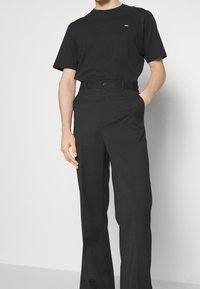 Černé bavlněné tričko s malým bílým logem, spárované s černými kalhotami s vysokým pasem a rovnými nohavicemi a zapínáním na knoflík.