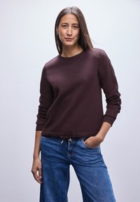 Felpa bordeaux con scollo a girocollo, polsini a costine e orlo con cordino, abbinata a jeans azzurri chiari, caratterizzati da una vestibilità comoda.