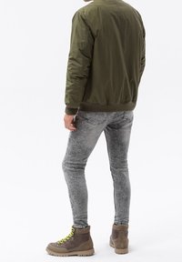 Olivgrön bomberjacka, slim fit grå jeans, bruna vandringsskor med gula snören. Mjuk material med ribbade mudd och midjeband.