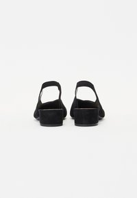 Chaussures en daim noir avec un talon bas et solide et un design à dos ouvert. La tige a une texture lisse et de simples accents de couture.