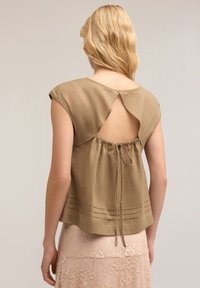 Khaki blouse featuring short sleeves, a rounded neckline, and an open back with a tie detail. Horizontal pleats near the hem.