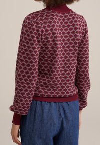 Bordeauxfärgad tröja med ett geometriskt diamantmönster i ljusrosa. Ribbad halsringning och manschetter, mjuk stickad textur, något avslappnad passform.